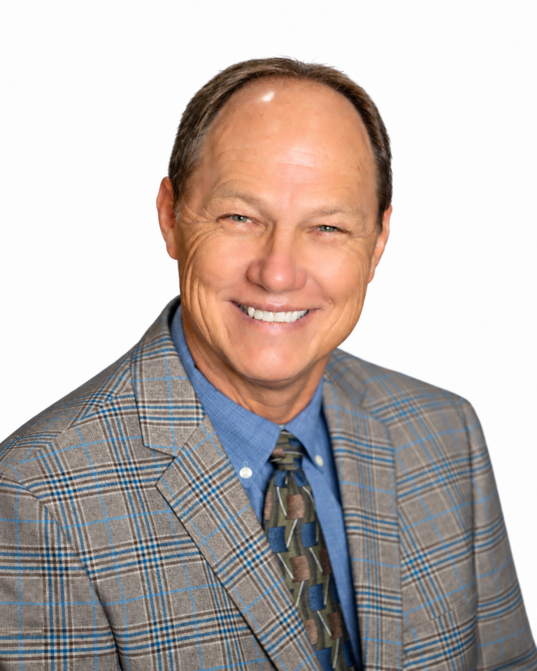A smiling middle-aged man wearing a blue button-down shirt, a patterned tie, and a blue and brown plaid blazer.